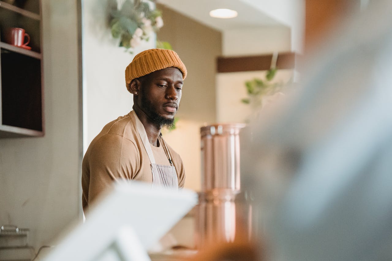 Barista in a warm café setting wearing a beanie and apron, providing excellent service.