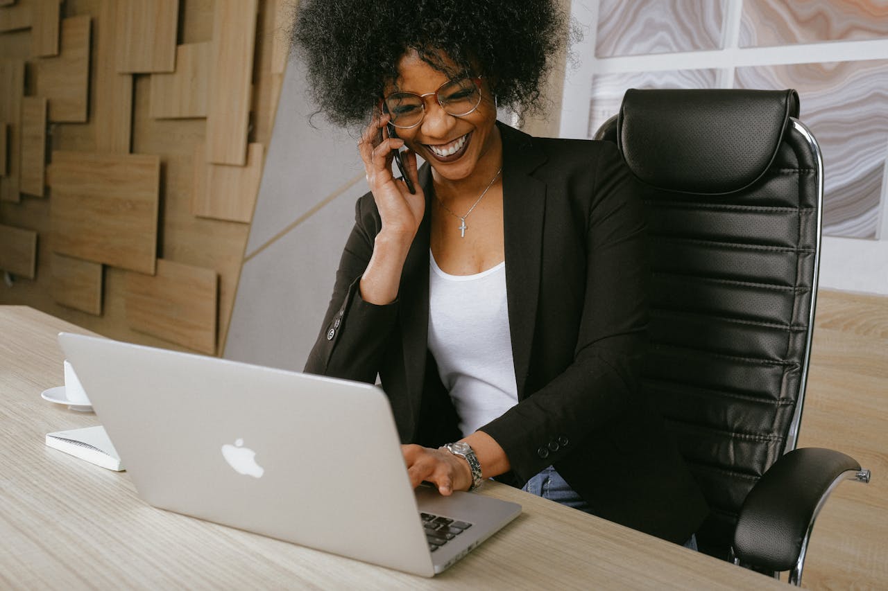 Smiling woman on phone call while working on a laptop in a stylish office.